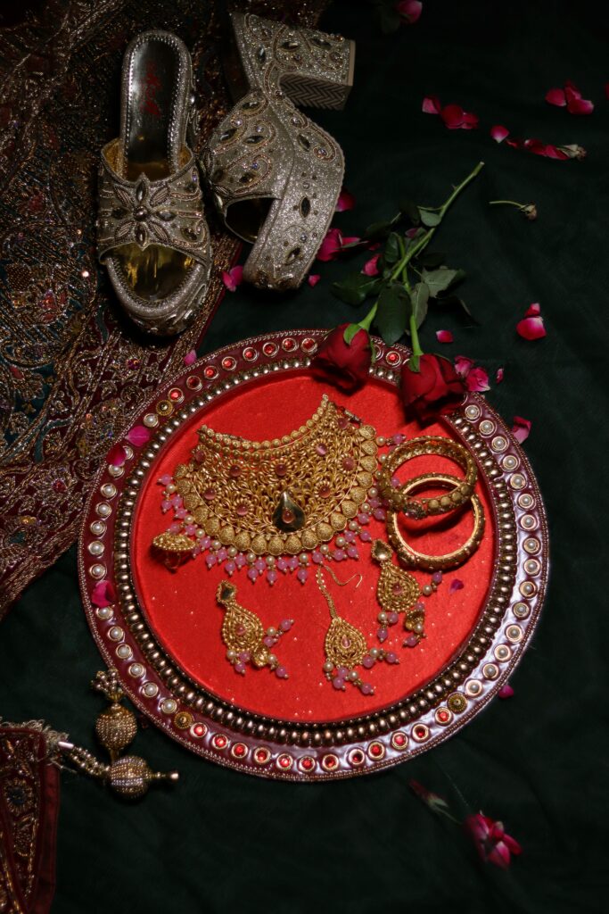 Flat lay of exquisite traditional jewelry set on a red velvet tray, adorned with flowers and footwear.